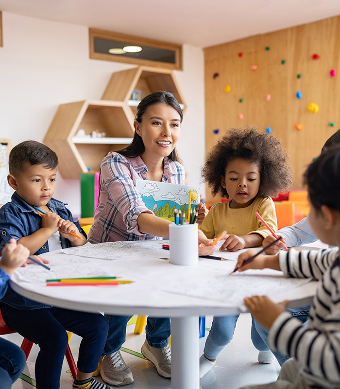 A teacher at a table with two young children, all drawing