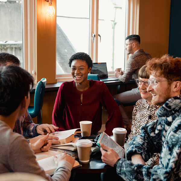Five people, mixed ages and ehtnicities, smiling and talking in a cofee shop