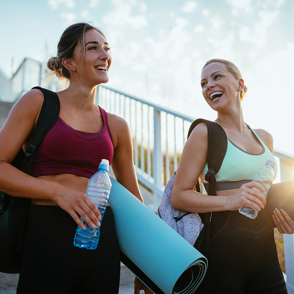 Two women smiling walking with yoga mats in hand