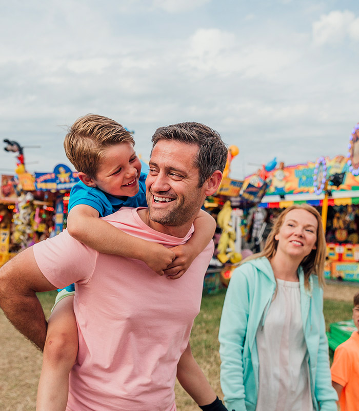 A young family of four walking, an amusement park in the background