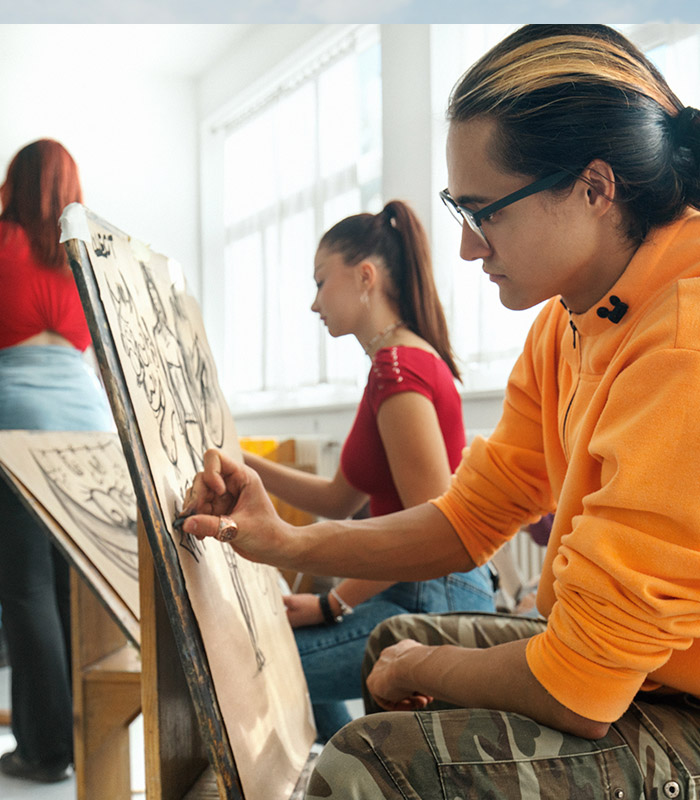 A man in the foreground painting on a canvas, with a women in the background also painting