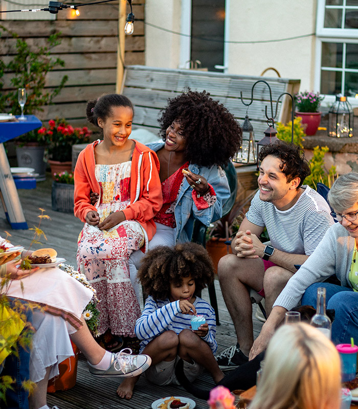 Four adults sat outside in a school garden, smiling and speaking with two young children who are on the floor eating