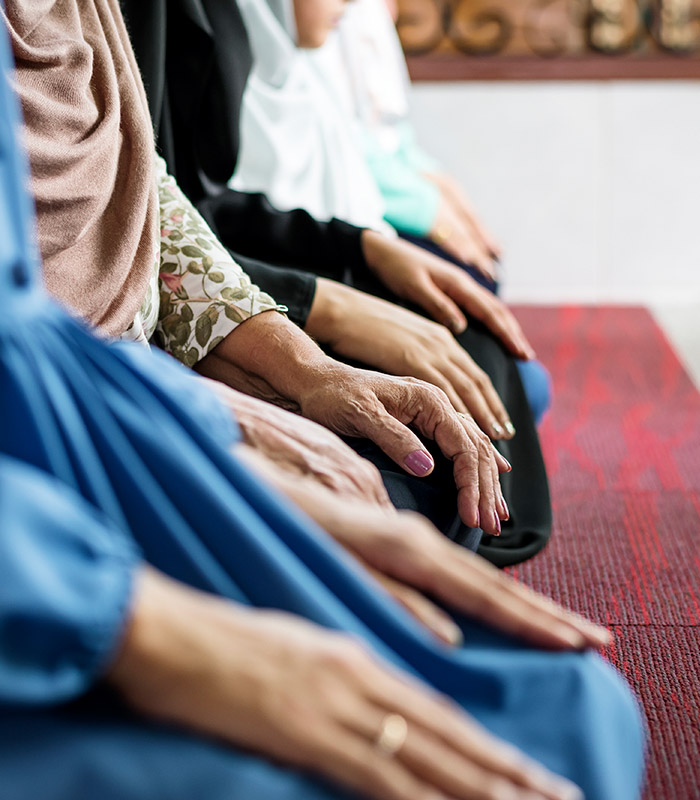 Women in a row wearing headscaves, knelt down praying